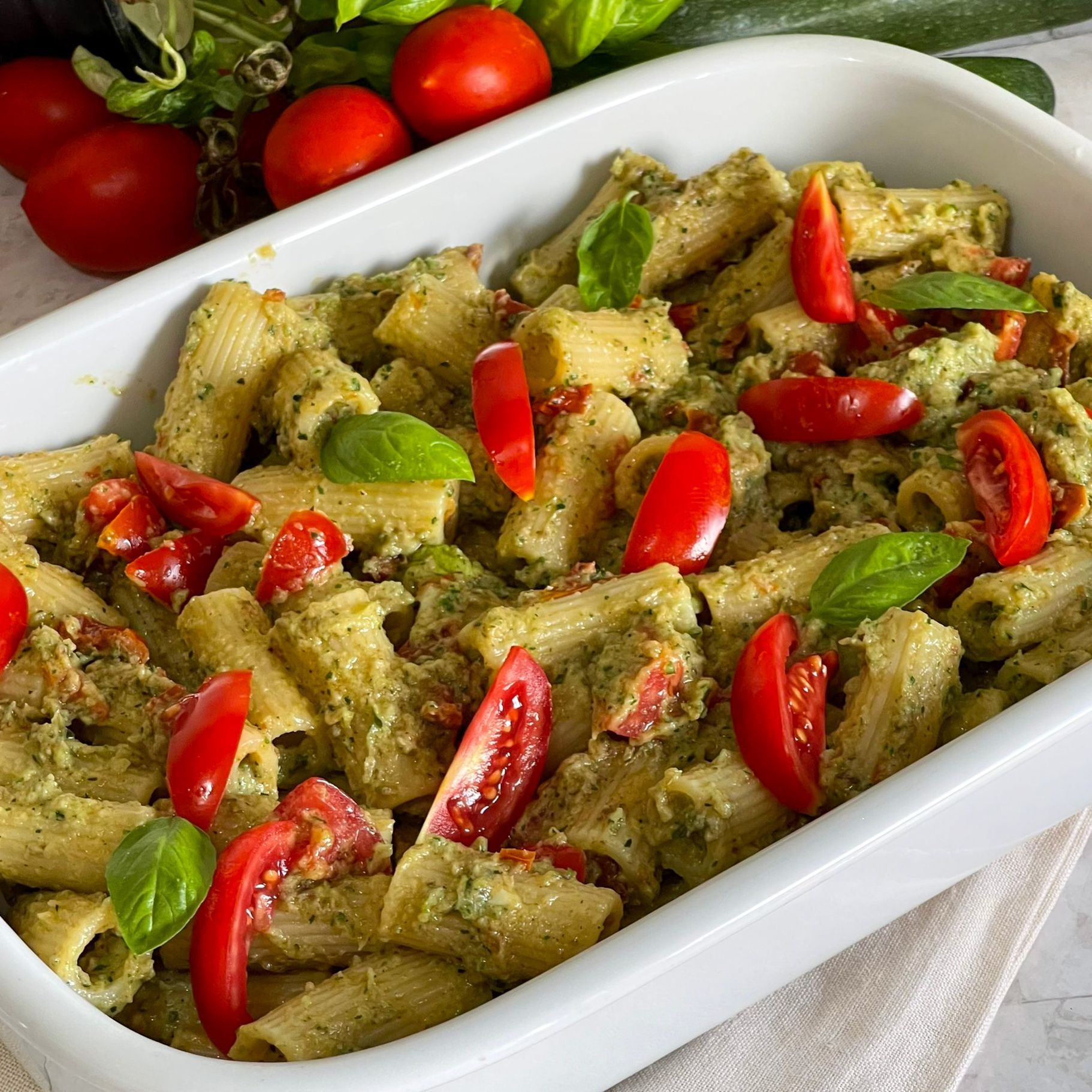 Una casseruola bianca piena di pasta, pomodori e basilico.