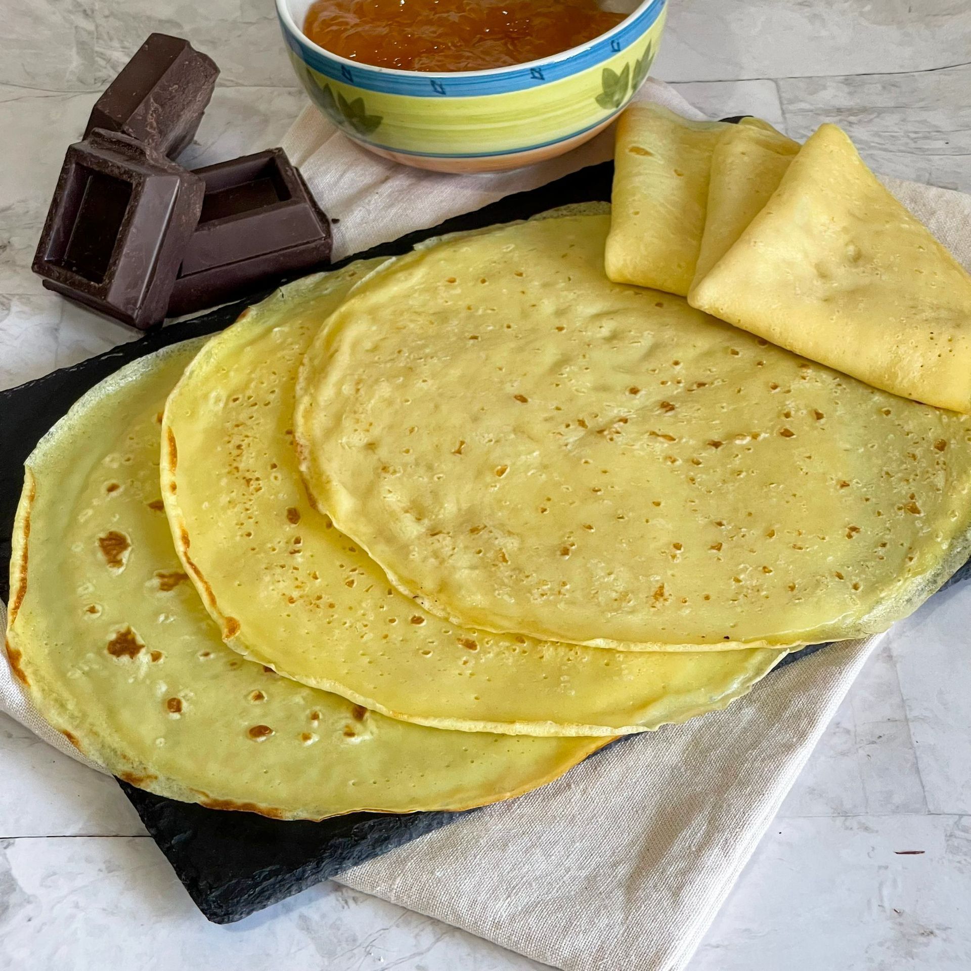 Tre pancake sono impilati uno sopra l'altro su un tavolo accanto a una ciotola di marmellata.