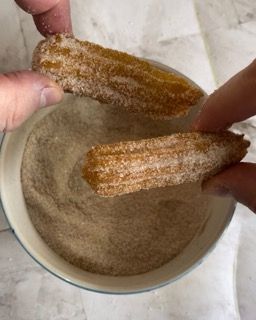 Una persona sta immergendo un churro nella polvere di cannella