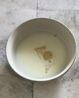 Una ciotola bianca piena di liquido è appoggiata su un tavolo.