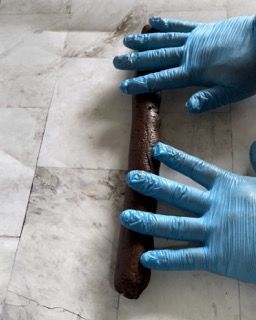 Una persona che indossa guanti blu sta arrotolando un pezzo di pasta al cioccolato