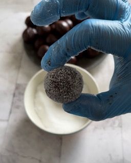 Una persona che indossa guanti blu tiene in mano una pallina di cioccolato.