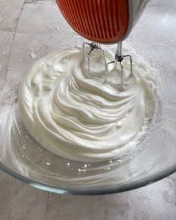 Uno sbattitore elettrico mescola la panna montata in una ciotola di vetro.