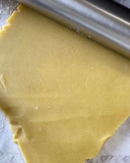 Un pezzo di pasta viene steso con il mattarello.