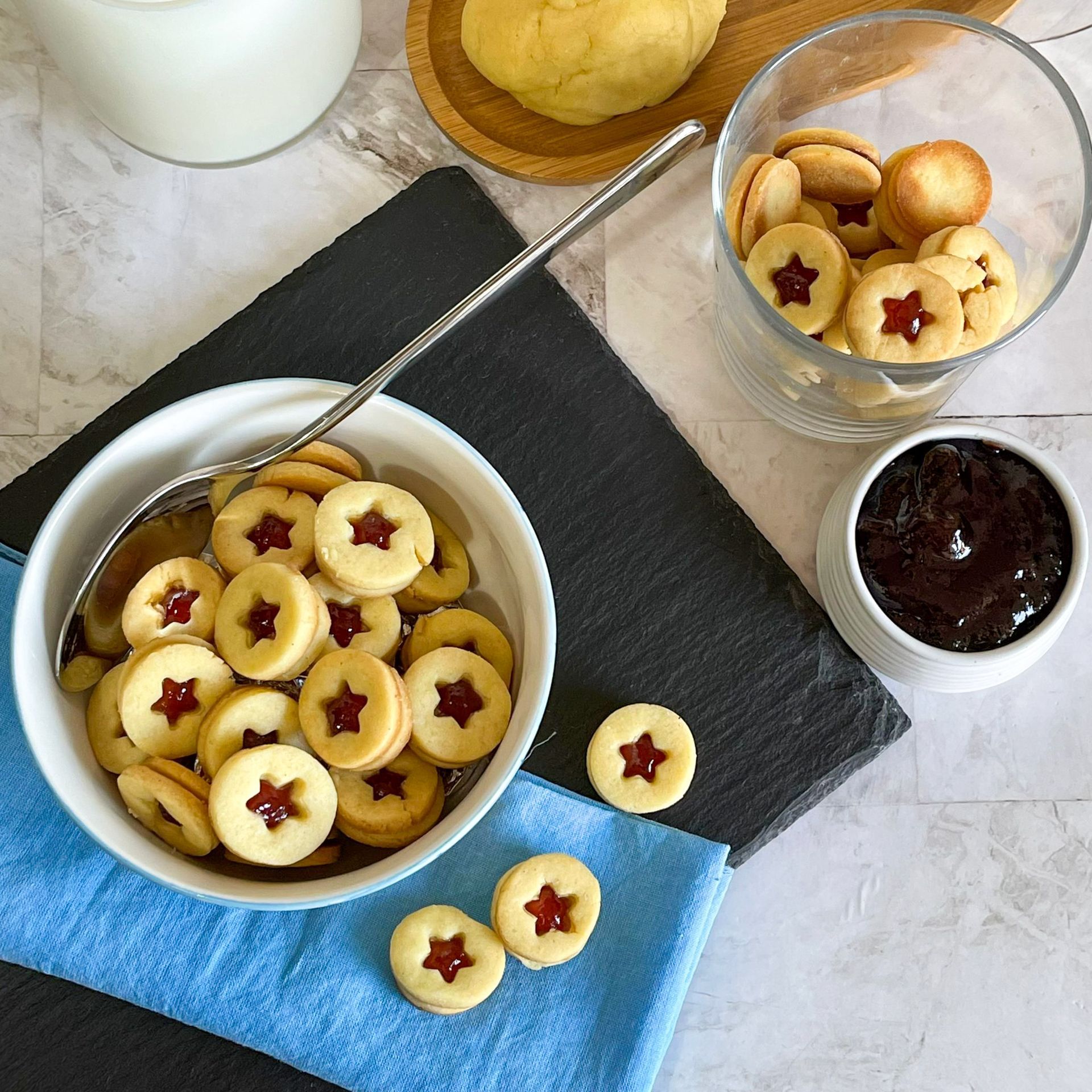 Una ciotola di biscotti con stelle rosse accanto a una ciotola di marmellata.