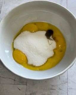 Una ciotola bianca piena di uova e zucchero su un tavolo