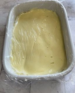 Una pirofila bianca piena di salsa gialla avvolta nella pellicola trasparente.