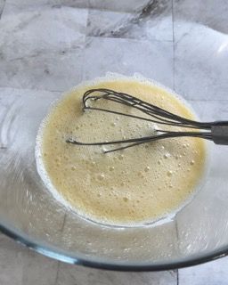 Una ciotola di vetro piena di un liquido giallo e una frusta.