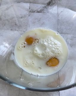 Una ciotola di vetro piena di latte e uova su un tavolo.