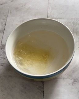 Una ciotola bianca piena di liquido è appoggiata su un tavolo.