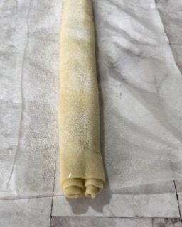 Un rotolo di pasta è appoggiato su un pezzo di carta oleata.
