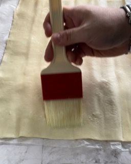 Una persona tiene un pennello sopra un pezzo di pasta.