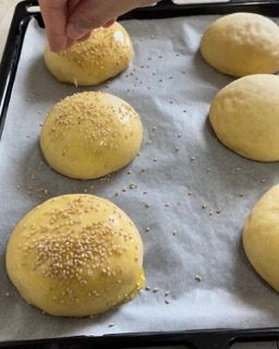 Una persona sta cospargendo semi di sesamo su alcuni panini