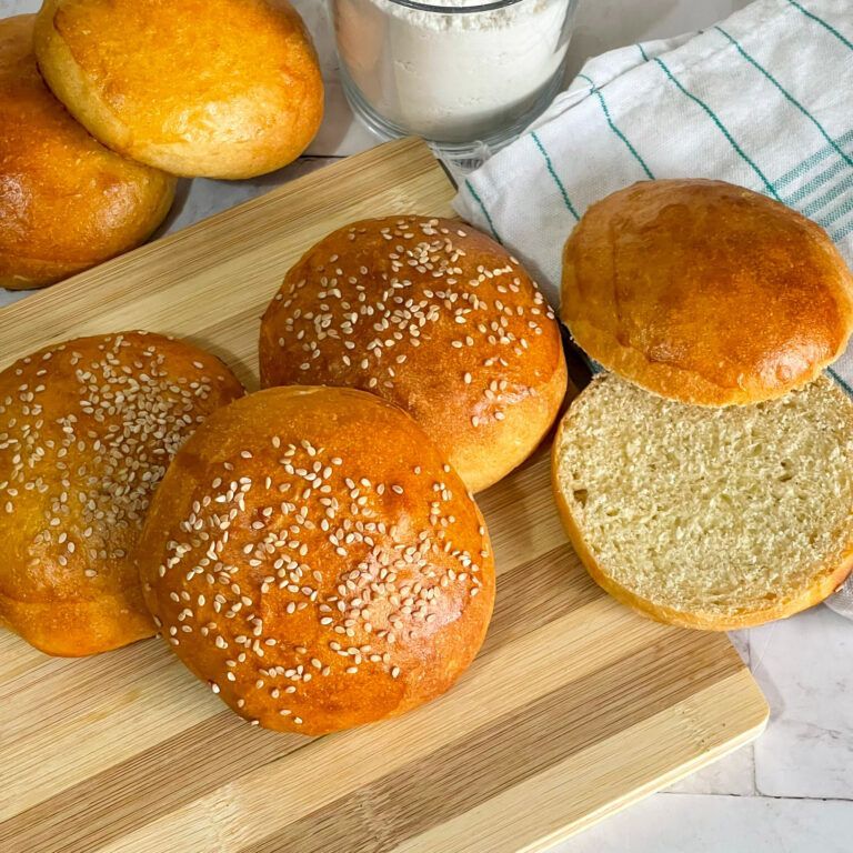Un mucchio di panini per hamburger con semi di sesamo su un tagliere di legno.