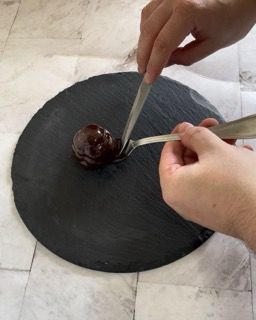 Una persona tiene una forchetta sopra una pallina di cioccolato su un piatto nero