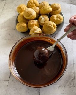 Una ciotola di salsa al cioccolato accanto a un piatto di bignè