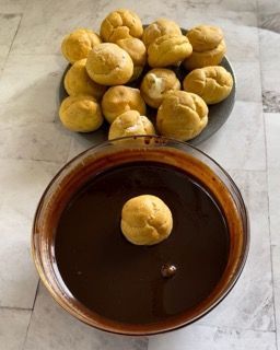 Una ciotola di salsa al cioccolato accanto a un piatto di bignè