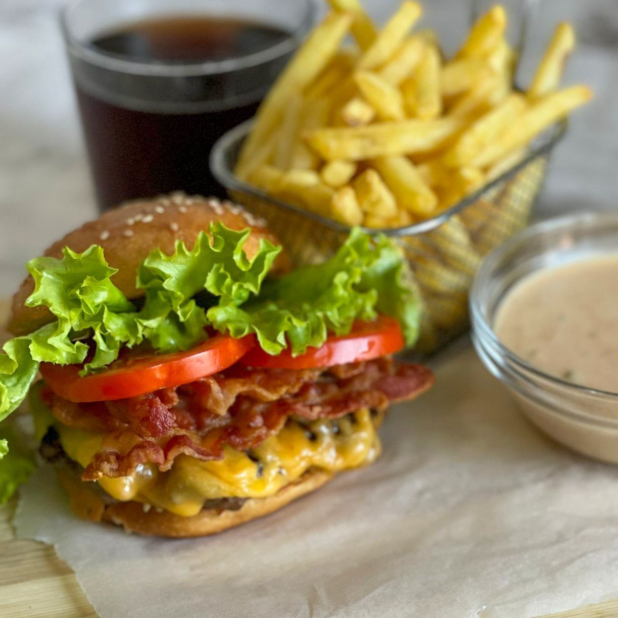 Un hamburger con lattuga, pomodoro e bacon accanto a un cestino di patatine fritte