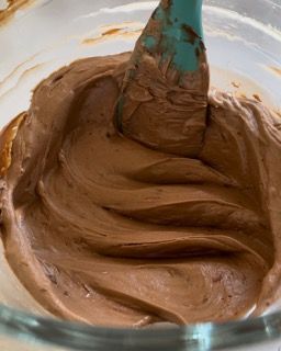 Una ciotola di glassa al cioccolato con una spatola dentro.