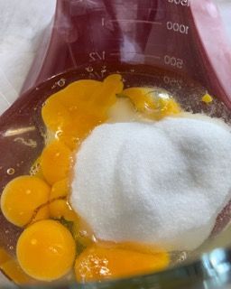 Un primo piano di uova e zucchero in una tazza graduata