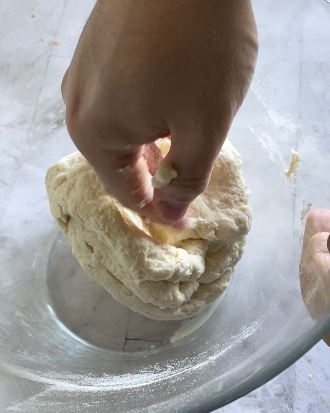 Una persona tiene in mano un pezzo di impasto in una ciotola di vetro.