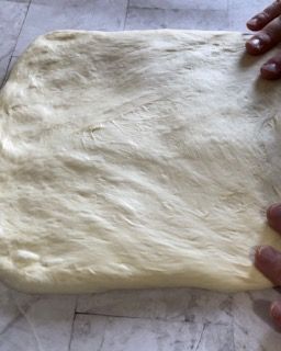 Una persona tiene in mano un pezzo di pasta su un tavolo.