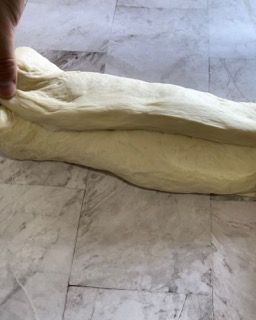 Una persona sta stendendo un pezzo di pasta su un pavimento piastrellato.