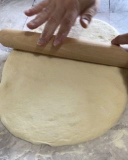 Una persona sta stendendo la pasta con un mattarello su un tavolo.