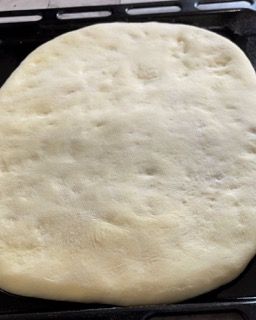 Un impasto per pizza è appoggiato su una padella nera.