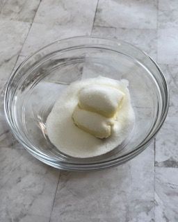 Una ciotola di vetro piena di burro e zucchero su un tavolo.