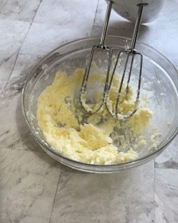 Una ciotola di vetro piena di panna montata accanto a un mixer