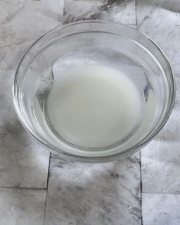 Una ciotola di vetro piena di liquido bianco è appoggiata su un tavolo.