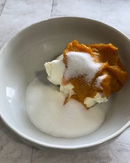 Una ciotola bianca piena di yogurt, purea di zucca e zucchero.