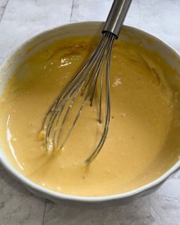 Una ciotola di liquido giallo con una frusta dentro.