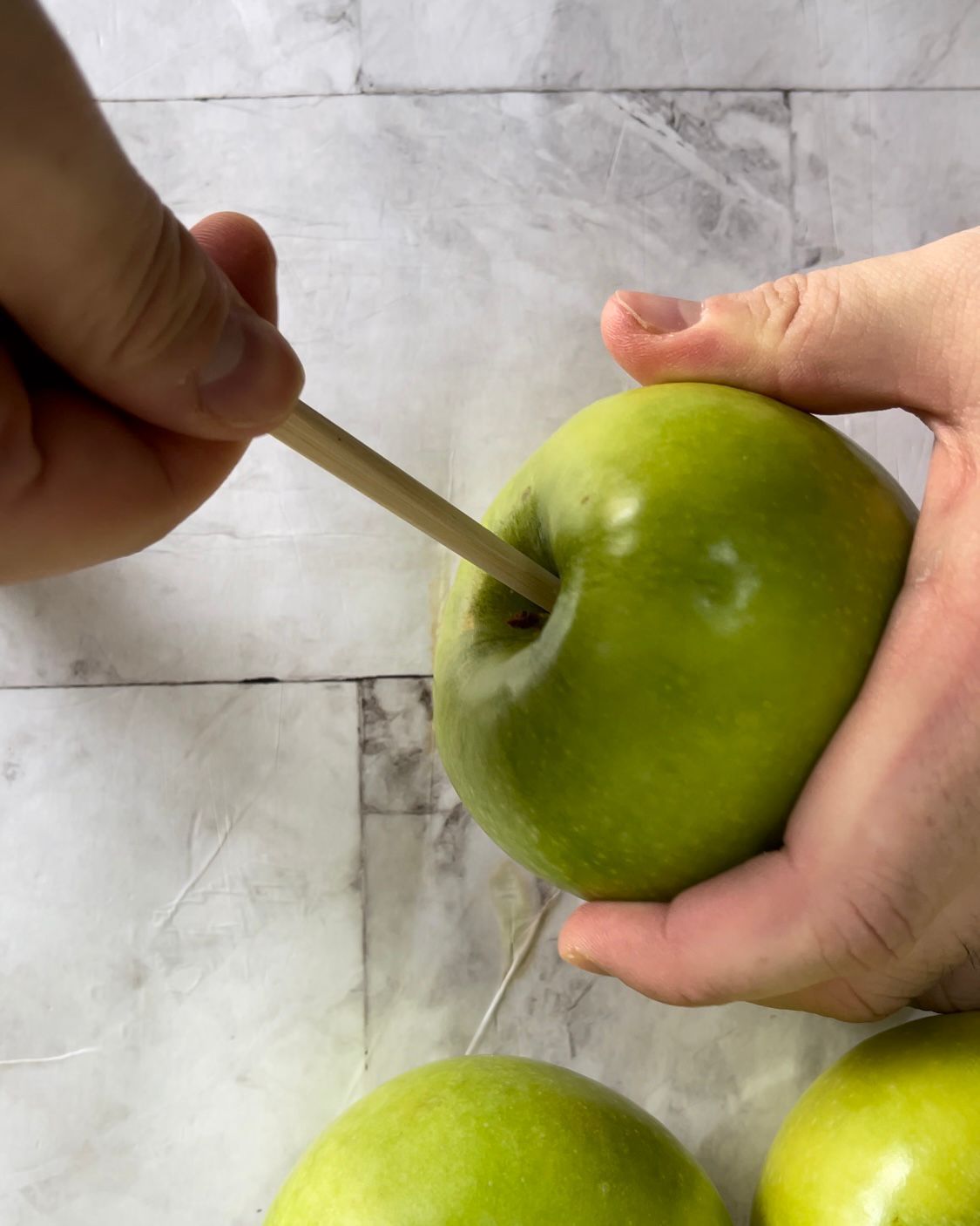 Una persona tiene in mano una mela verde con uno stuzzicadenti infilato.
