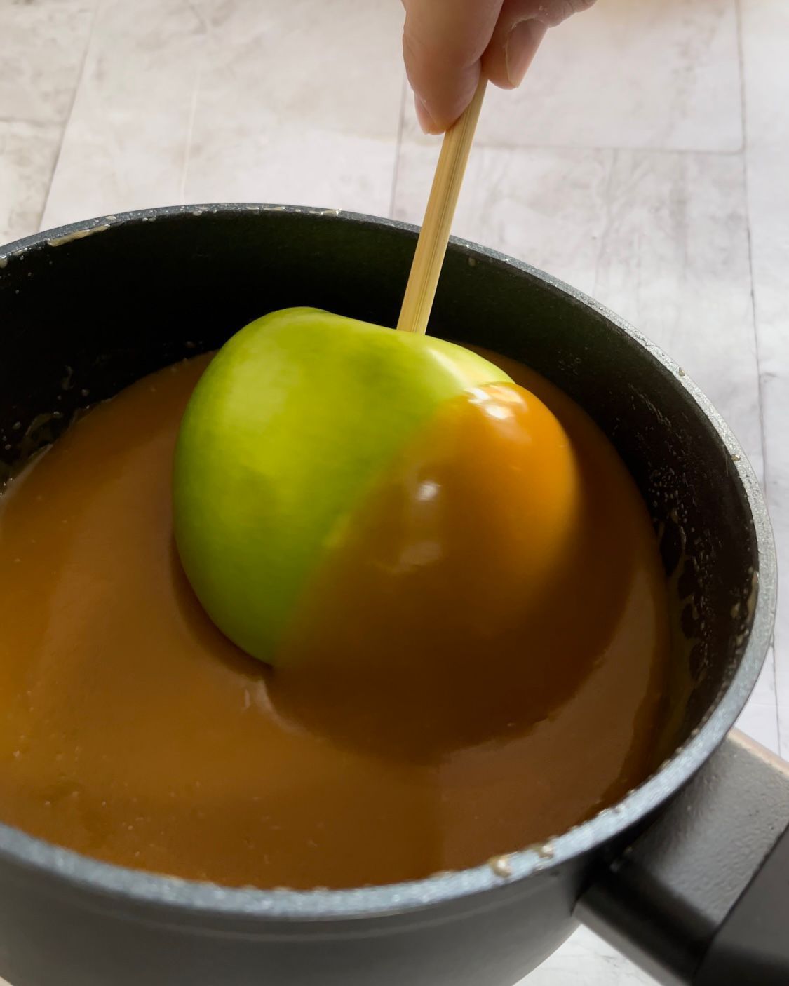 Una persona sta immergendo una mela verde nella salsa al caramello