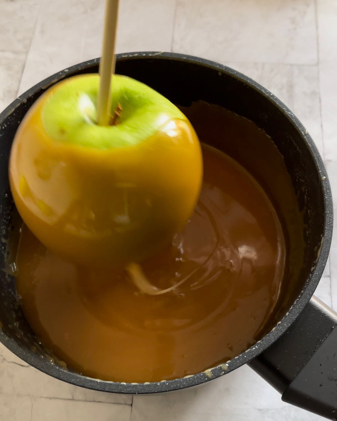 Una mela verde su un bastoncino in una pentola di caramello