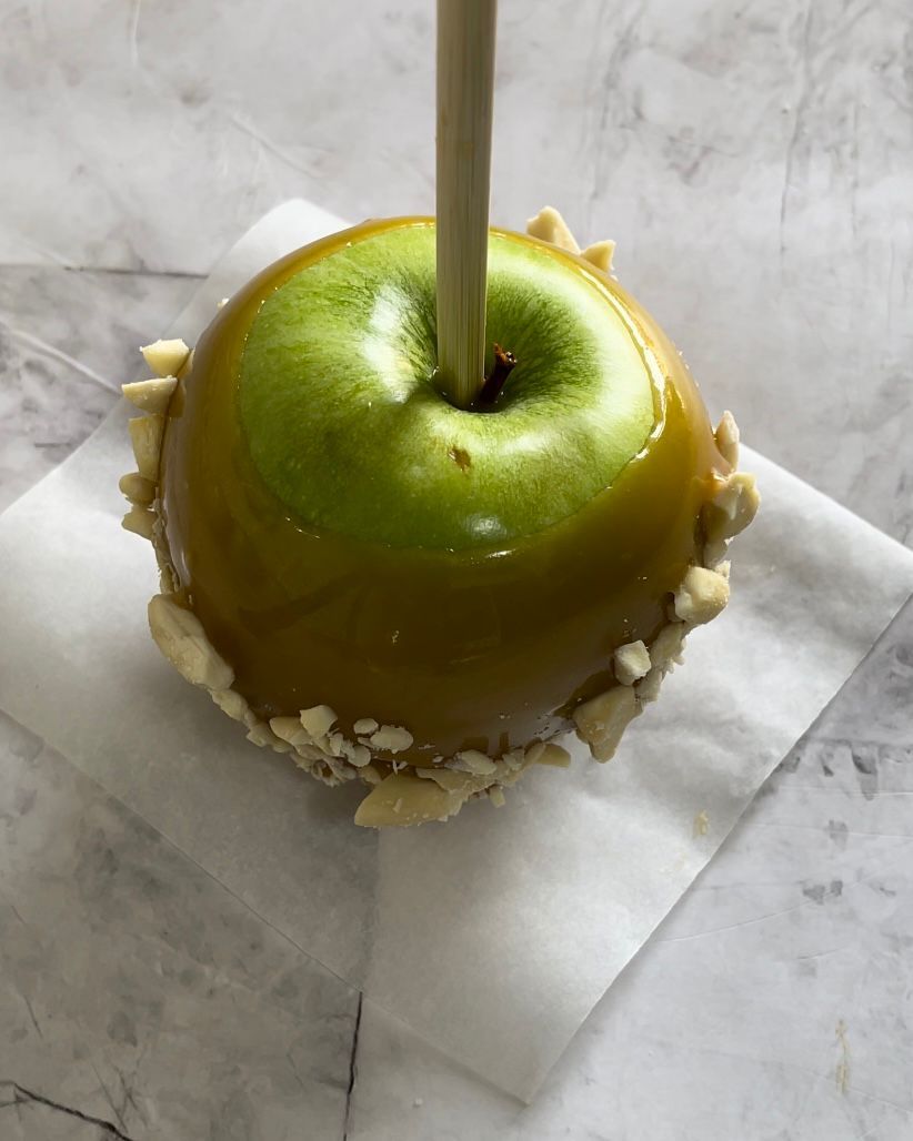 Una mela caramellata verde con un bastoncino che sporge da essa