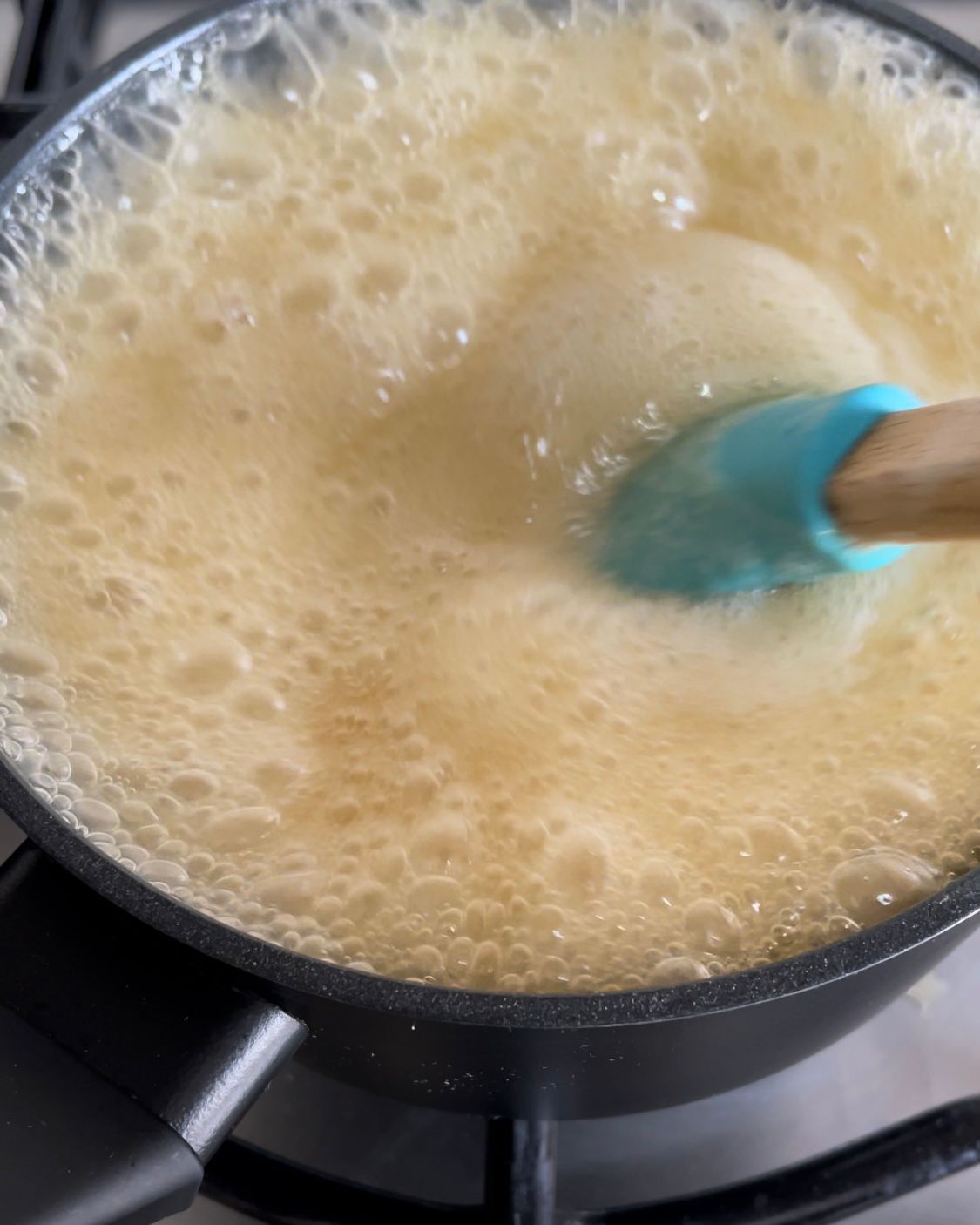 Una pentola piena di liquido viene mescolata con una spatola su un fornello.