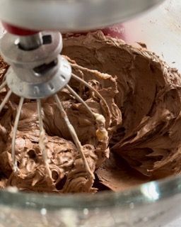Un mixer sta mescolando la glassa al cioccolato in una ciotola di vetro