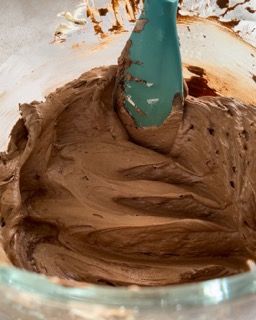 Una ciotola di glassa al cioccolato con una spatola blu dentro.