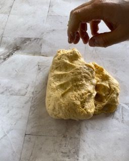 Una persona tiene in mano un pezzo di pasta su un tavolo.