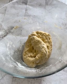 Una ciotola di vetro piena di impasto è appoggiata su un tavolo.