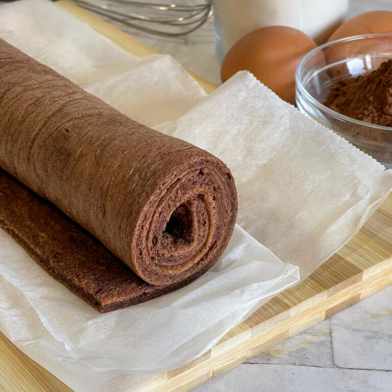 Un rotolo di cioccolato è appoggiato su un pezzo di carta oleata su un tagliere di legno.