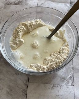 Una ciotola di vetro piena di farina e latte con un cucchiaio dentro.