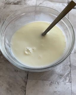 Una ciotola di vetro piena di liquido bianco e un cucchiaio dentro.