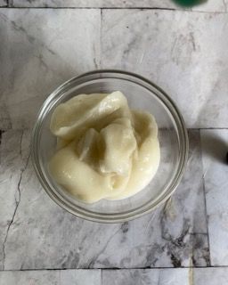 Una ciotola di vetro piena di un liquido bianco su una superficie di marmo.