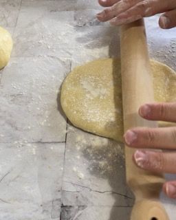 Una persona sta stendendo la pasta con un mattarello su un tavolo.