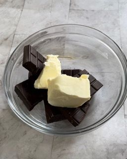 Una ciotola di vetro piena di cioccolato e burro su un tavolo.