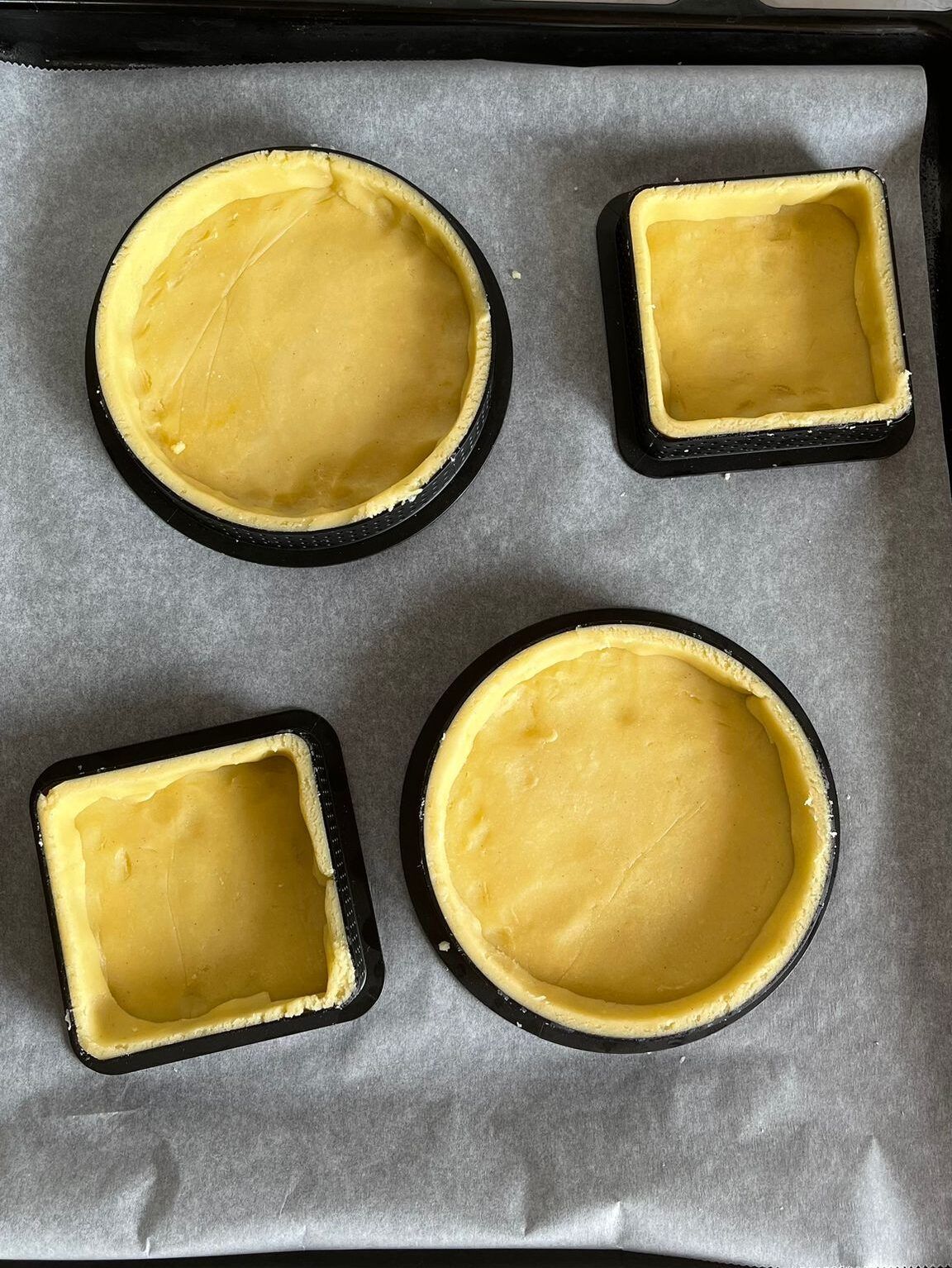 Quattro gusci di crostata sono adagiati su una teglia da forno ricoperta di carta da forno.